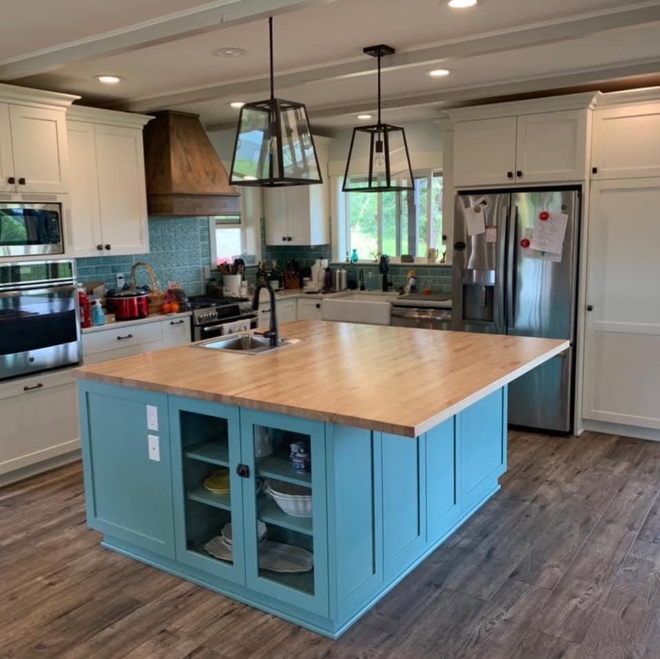 Remodeled kitchen with white shaker cabinets, a teal island with a butcher-block counter, tile backsplash, and a wood vent hood cover